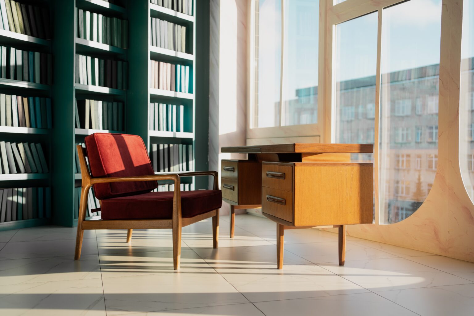 Sonniges Arbeitszimmer mit bordeauxrotem Sessel und Nussbaumschreibtisch neben hohen Bücherregalen