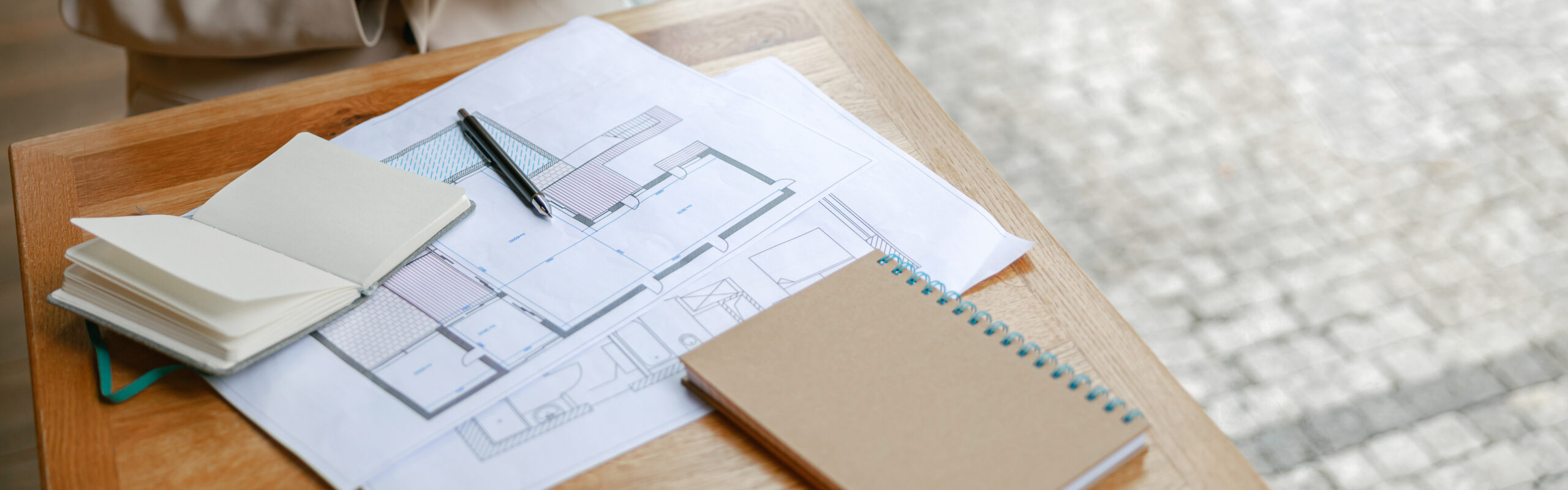 Architektonische Grundrisse mit Notizbüchern und einem Stift auf einem Holzschreibtisch