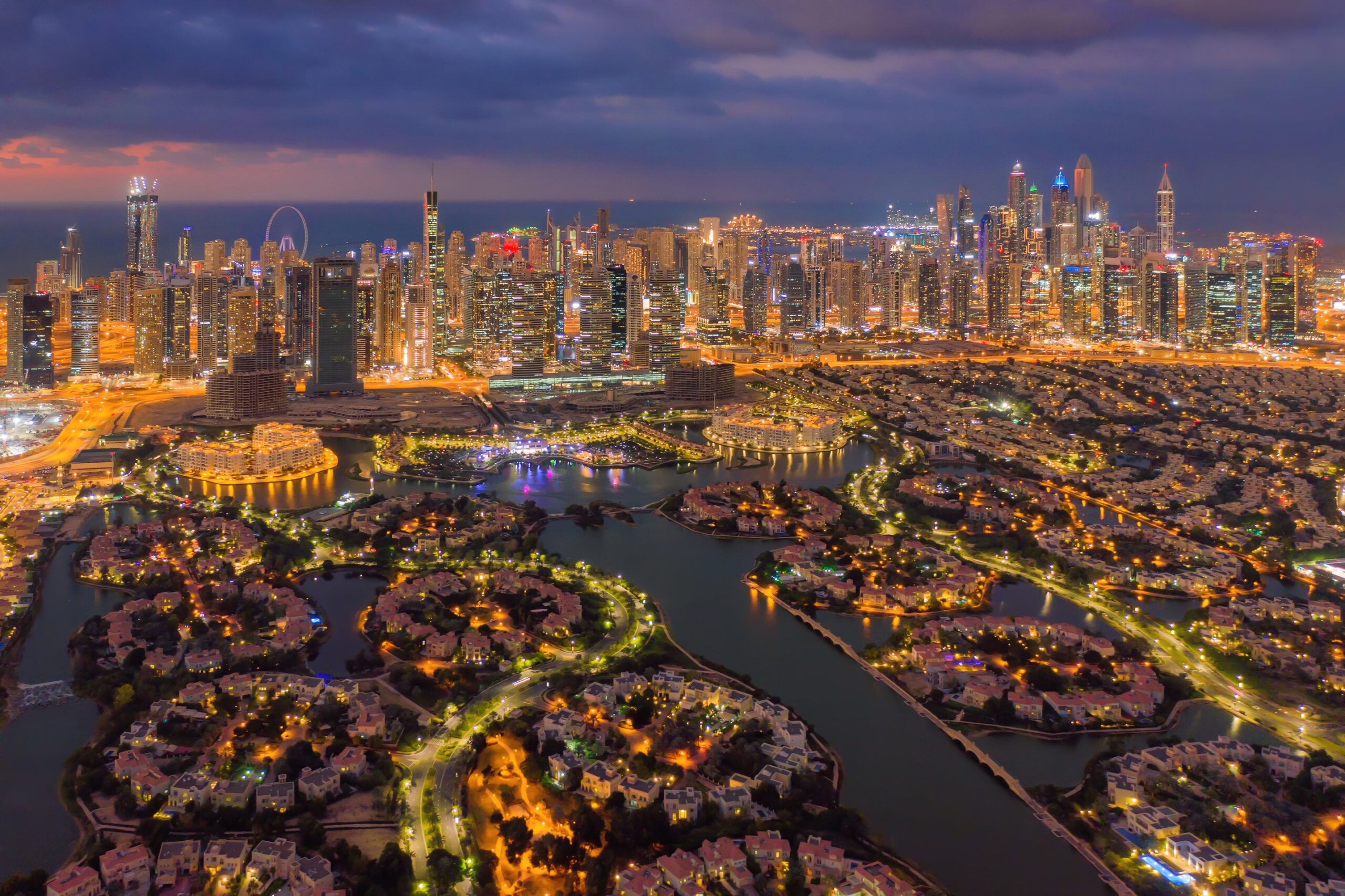 Комплексы вилл и каналы в вечерних огнях, вдали силуэт Dubai Marina и JLT