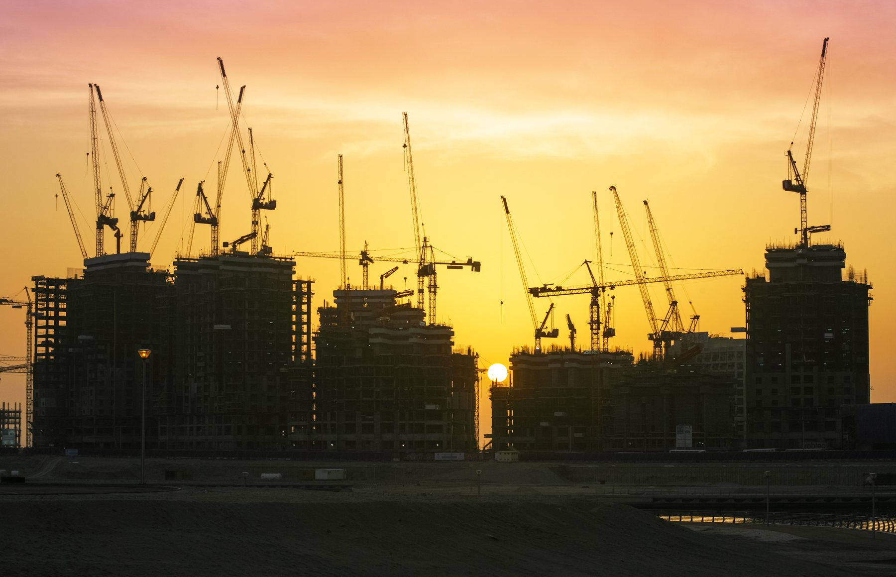 Towers under construction with tower cranes silhouetted against a Dubai sunset