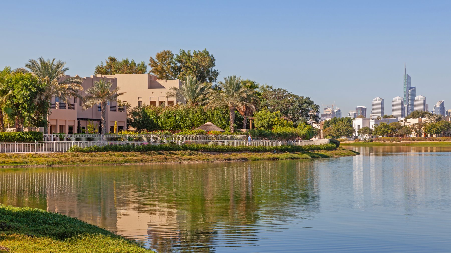 Private villas among palms on a lake in Dubai, with towers beyond